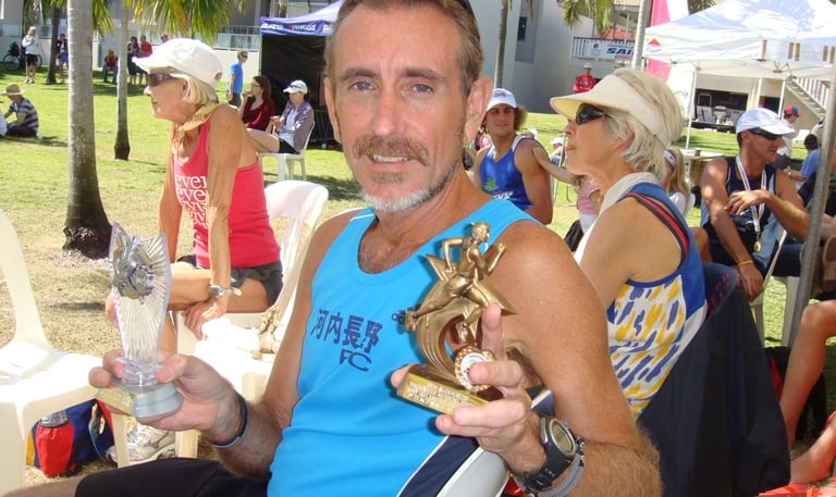 Coach Scott Brown holding two trophies from the Townsville marathon.