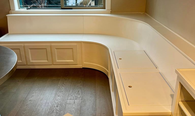 Custom white built-in window seat with storage and curved corner bench seating in a home.