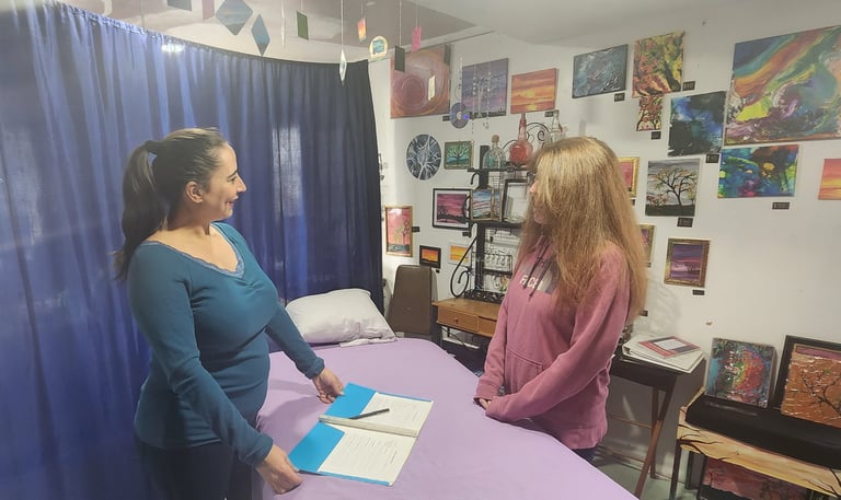 A Reiki therapist consults with a client in a studio decorated with colorful art and paintings.