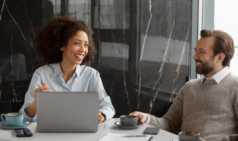 a man and woman sitting at a table with a laptop