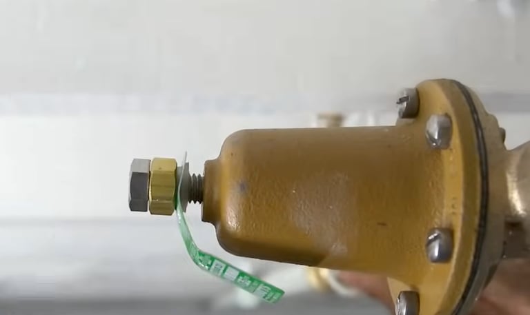 Close-up of a yellow water pressure reducing valve with brass adjustment bolt and safety seal.
