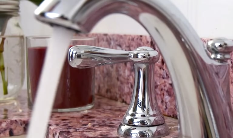 Polished chrome bathroom faucet running water over a pink granite countertop.