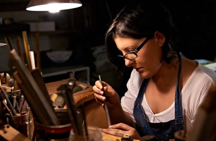 Una joyera experta talla detalles intrincados en metal en el banco de trabajo de su estudio.
