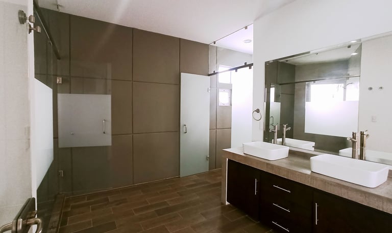 baño de recámara principal con espacios independientes y cancelería en cristal
