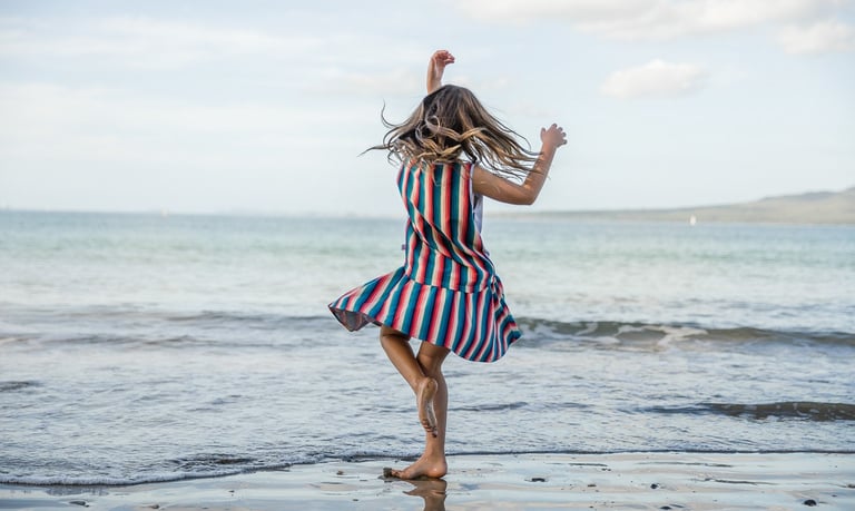 Fashion photography - a girl in a striped dress dancing on the beach