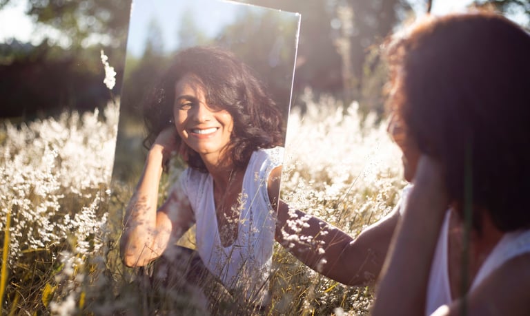 woman looking at herself in mirror while sitting in open field