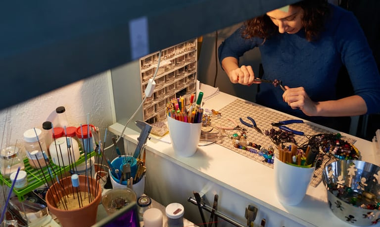oyero utilizando pinzas para elaborar collares de cuentas artesanales en una mesa de trabajo.