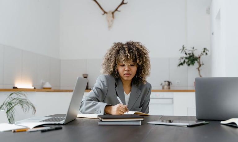Black woman sitting at a desk and writing in a notebook 