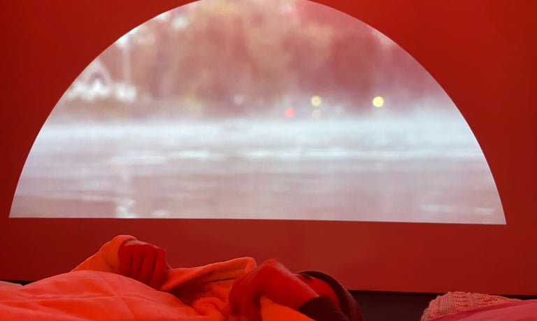 Person lies in bed under a blanket with a thermal lake projection on a half-moon screen behind them.
