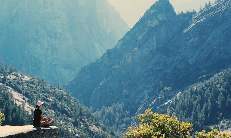 Longevity Travel - a person sitting on a rock with a mountain in the background