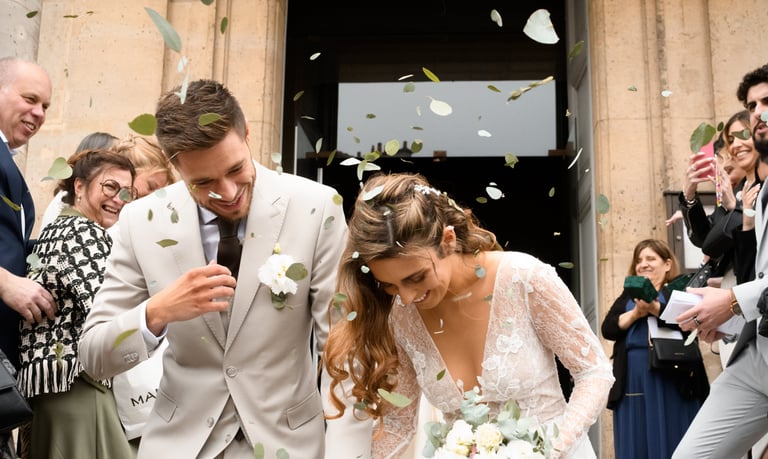 La mariée et le marié sous un jeté de pétales et de fleurs, à la sortie de l'église