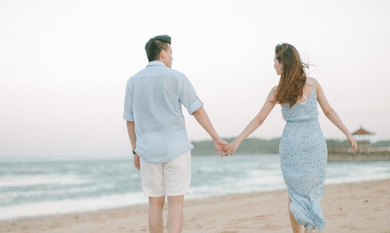 Intimate couple walking hand in hand along shoreline at Sofitel Bali Nusa Dua Beach Resort.
