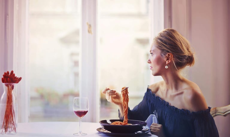 A woman enjoying a bowl of spaghetti in tomato sauce and glass of red wine