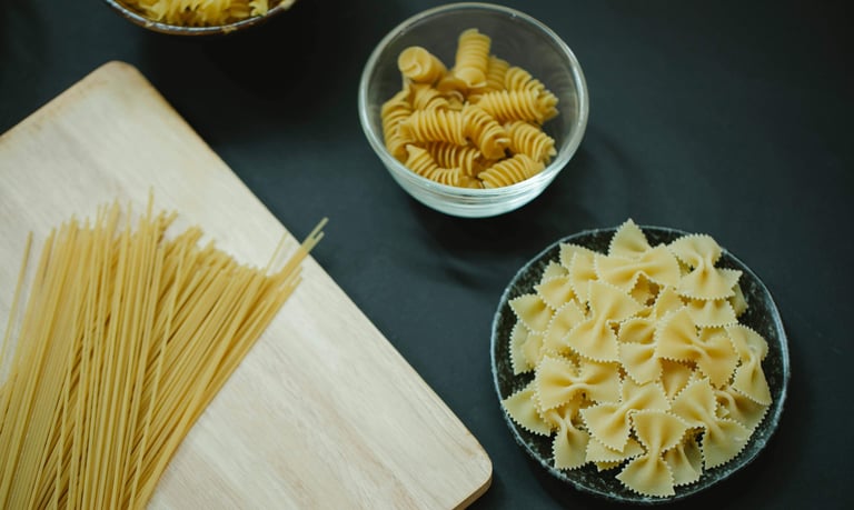 An assortment of pasta (spaghetti, fussili, and farfalle) on a table
