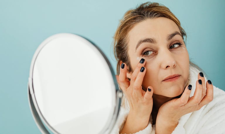 A woman applying eye cream in front of a mirror