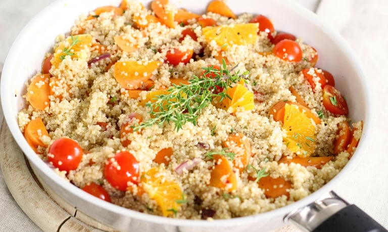 Quinoa salad with tomatoes, orange segments, carrots, and rosemary.