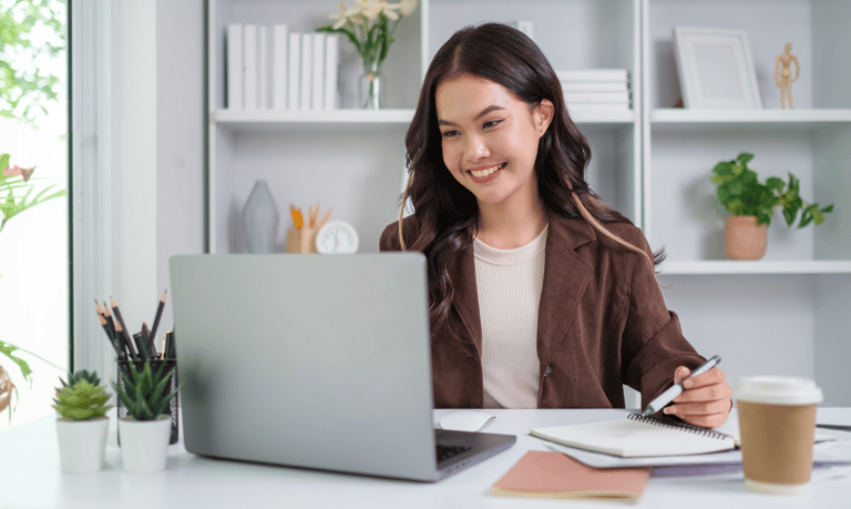 Chica sonriente sentada en un escritorio con un ordenador portátil y una libreta