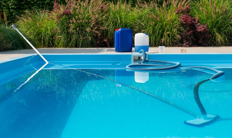 Pool cleaning hose chemical containers water testing kit beside a clear blue swimming pool.