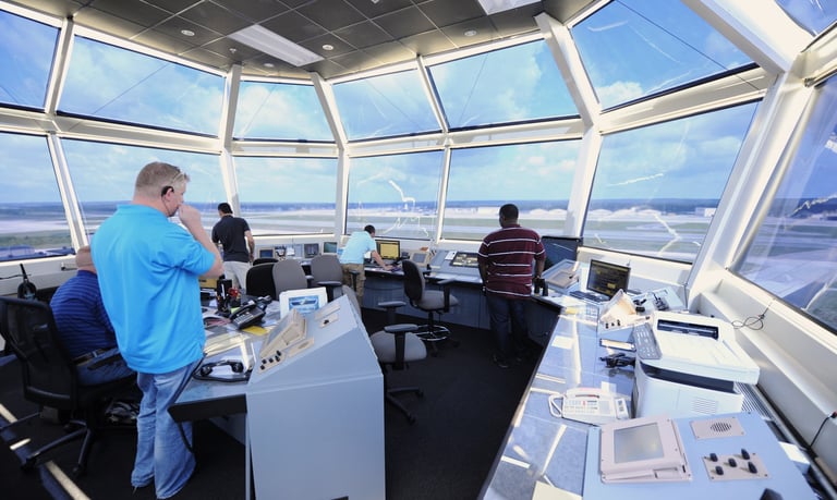 a man in a blue shirt is standing in front of a large window in an airport control tower