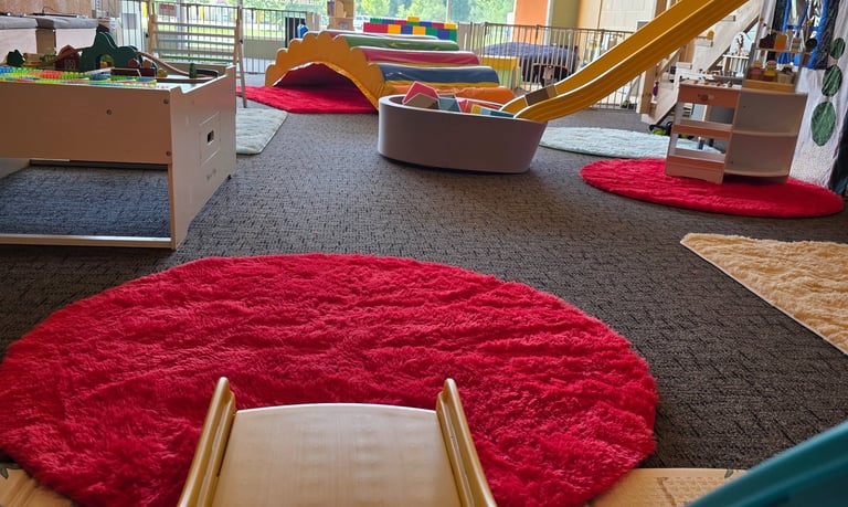 Indoor playground for toddlers featuring colorful slides, soft play mats, a train table, and more.