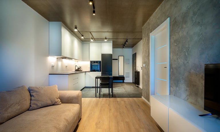 Nowoczesny salon z aneksem kuchennym, jasne meble, betonowy sufit i ściana TV.