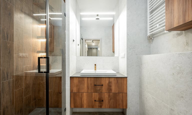 Nowoczesna łazienka z umywalką na szafce, lustrem, kabiną prysznicową i grzejnikiem.