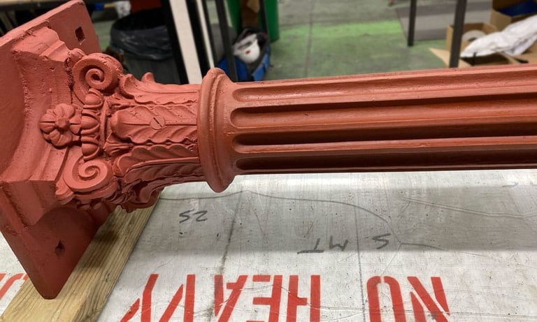 A red primed Victorian metal column and capital lying on table in industrial setting.