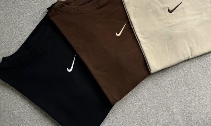 Tres sudaderas Nike de cuello redondo dobladas en colores neutros.
