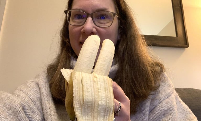 a woman in glasses and a sweater is holding a banana peeler