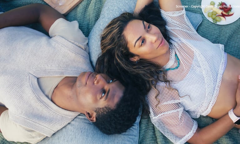 A young couple relaxing on a picnic blanket with fresh fruit snacks outdoors.