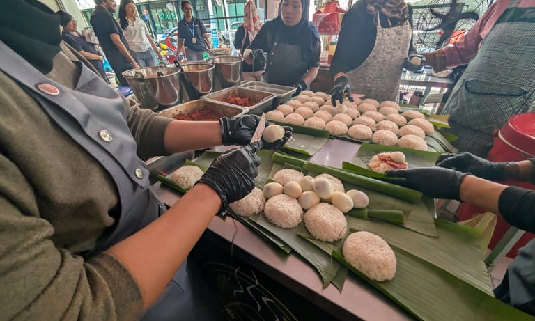 Street food vendors preparing traditional Nasi Lemak on banana leaves with rice and boiled eggs.