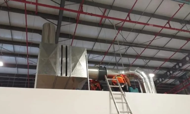 Técnicos de HVAC instalando una caja de filtrado de acero galvanizado en una maquiladora