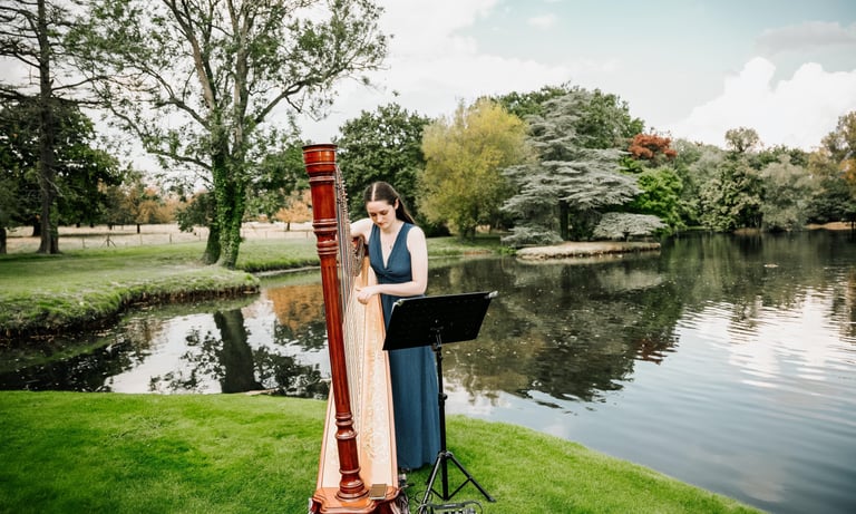 Harpist performing by a lakeside during an outdoor wedding.