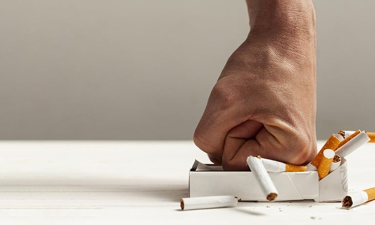 un poing qui écrase un paquet de cigarette