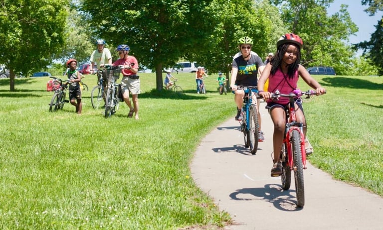 Two people riding bikes on a paved path through a green space