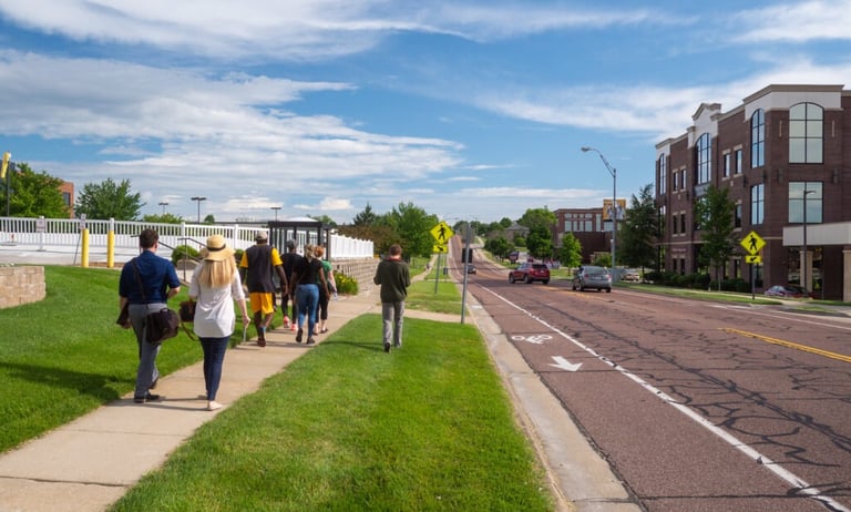 Crowd of people walking on a sidewalk next to a busy road