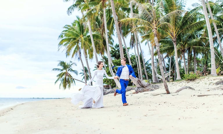 Wedding couple running on Ong Lang Beach under palms
