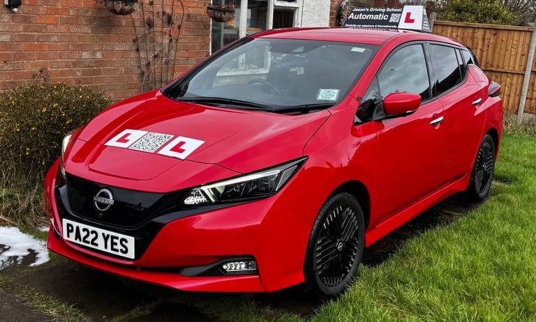 Red Nissan Leaf automatic driving school car with L-plates parked on a driveway for driving lessons.