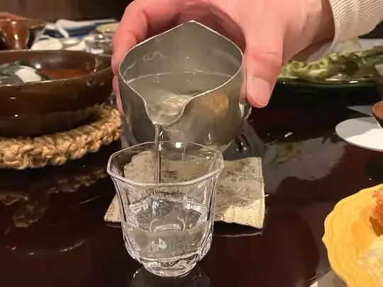 Sake being poured from a metal tokkuri into a crystal glass at a Kyoto restaurant