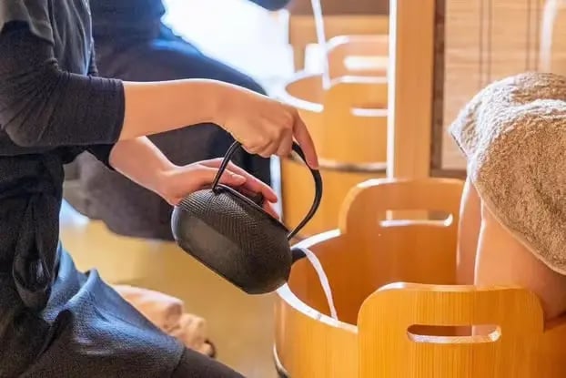 Cast iron kettle pouring warm water into wooden foot bath tub at Japanese spa