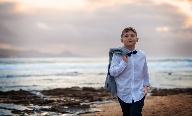 a young boy in a white shirt and tie dye on a beach