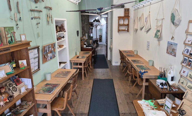 Dalbeattie Wood workshop with wooden work tables and chairs against opposite walls and various items on the walls.
