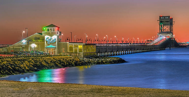 James River Bridge and restaurant at sunset with vibrant orange and purple sky over calm water.