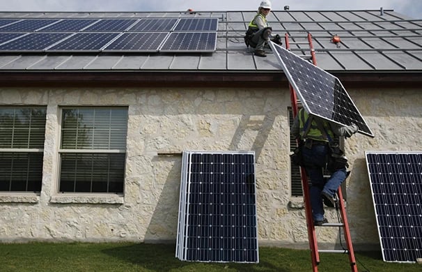Professional solar installers mounting high-efficiency photovoltaic panels on a residential metal roof.