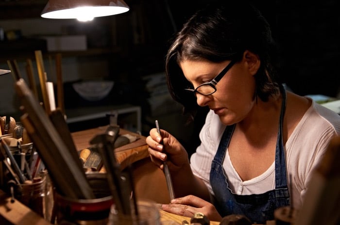 artesana grabando un anillo hecho a mano bajo una lámpara de escritorio en su taller
