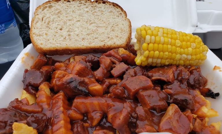 Smothered BBQ turkey fries with corn on the cob and a slice of bread in a takeout container.