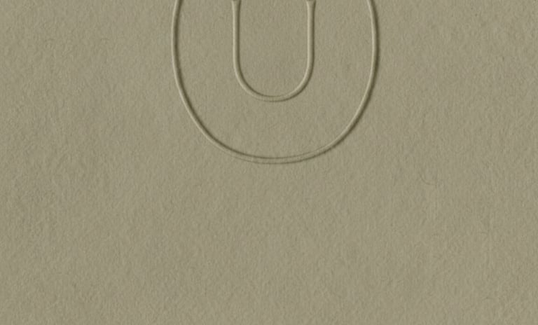 Logotipo minimalista en relieve que presenta una U con un circunflejo dentro de un óvalo.