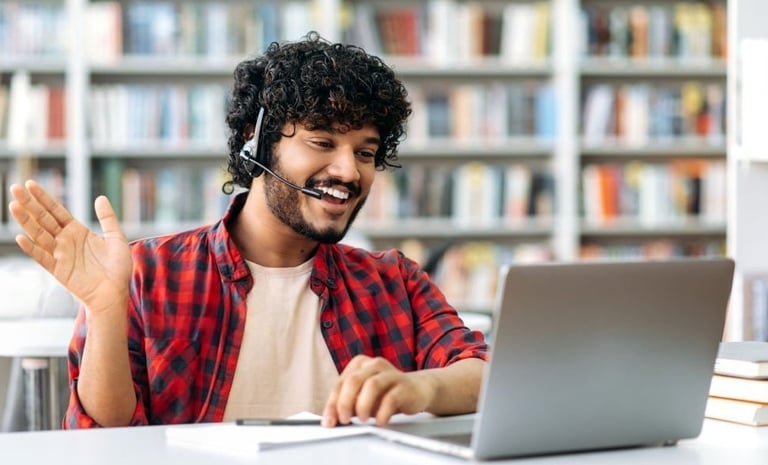 Male student with headset waving in front of laptop