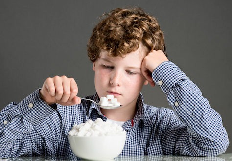 a boy eating cubes of sugar in spoon from glass bowl