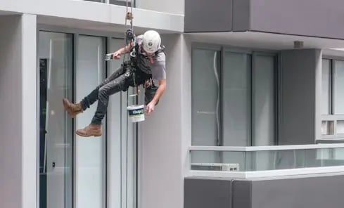 Artisan façadier de DM Rénovation effectuant un ravalement de façade sur cordes sur un immeuble à Landivisiau